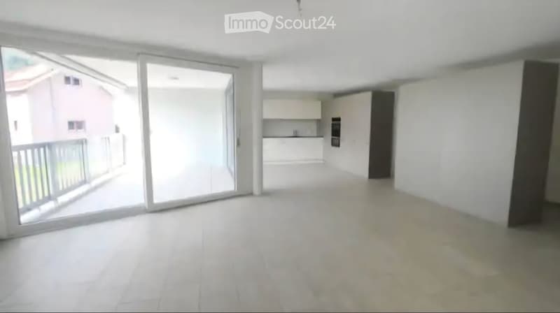 Empty living space with white walls, large sliding glass doors leading to a balcony, and a view of a neighboring building.
