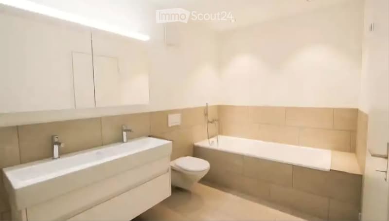 Modern bathroom with a white sink, bathtub, and toilet. Light-colored tiles and cabinetry.