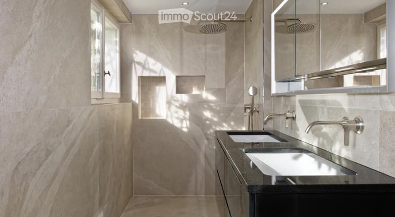 Modern bathroom with beige stone tiles, double sink vanity, large mirror, and a walk-in shower with a glass enclosure.