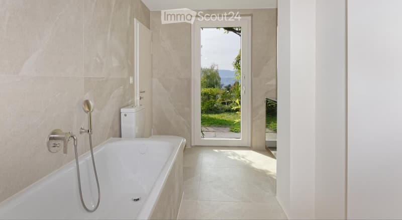 Modern bathroom with a bathtub, toilet, and a large window offering a scenic view of greenery and mountains.