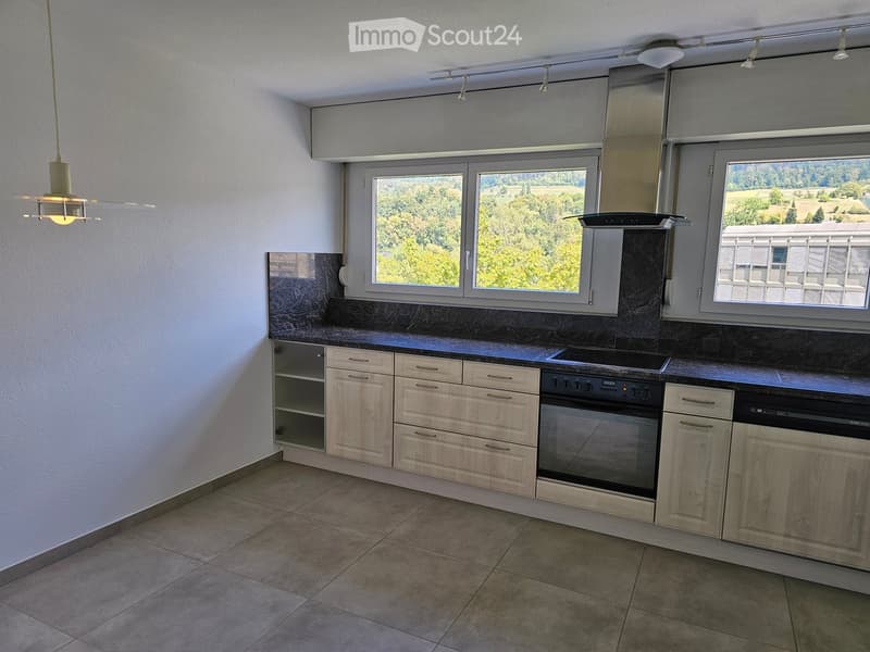 Modern kitchen with light wood cabinets, stainless steel appliances, and large windows offering a scenic view.