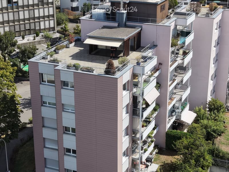 Aerial view of a modern multi-story residential building with multiple balconies, greenery, and outdoor seating areas.
