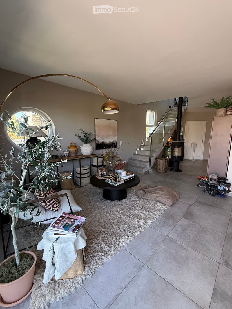 Modern living room with a large, round floor lamp, a cozy sofa with throw pillows, a coffee table with books and decorative items, a shaggy white rug, and a staircase leading to an upper level.