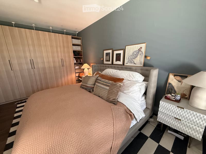 Modern bedroom with a large bed, nightstand, lamp, wardrobe, and picture frames on the wall.