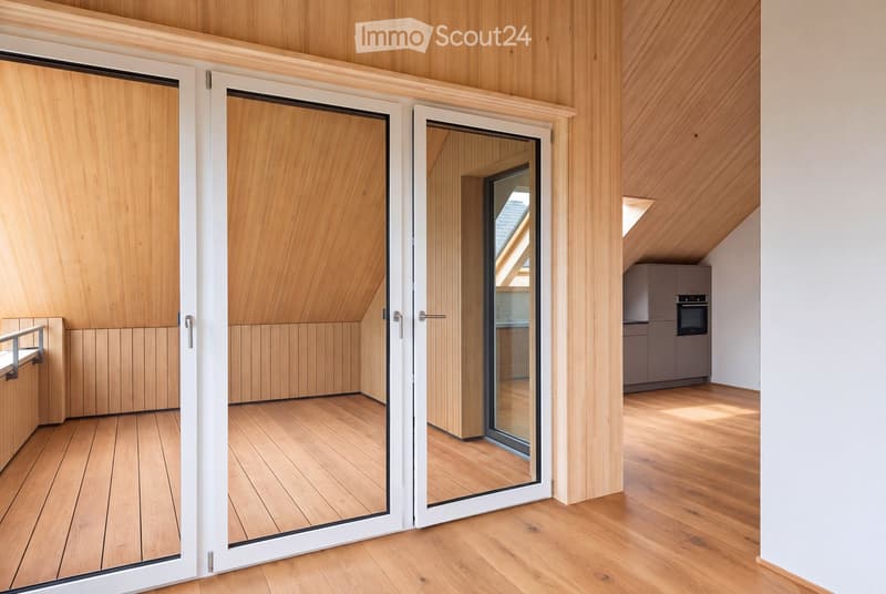 Modern, minimalist interior with wooden walls and flooring, featuring a large sliding glass door leading to a balcony area and a compact kitchen with grey cabinets and an oven.