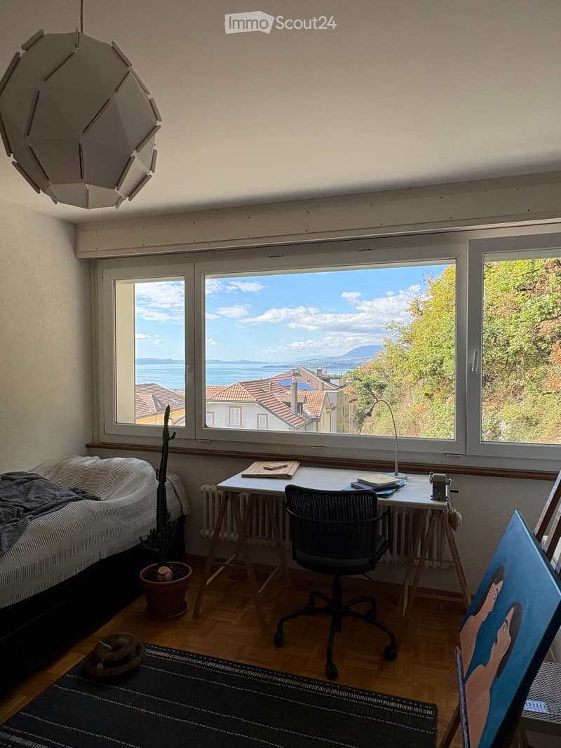 Bright room with large windows offering a scenic view, furnished with a sofa, desk, chair, lamp, and a painting on the wall.