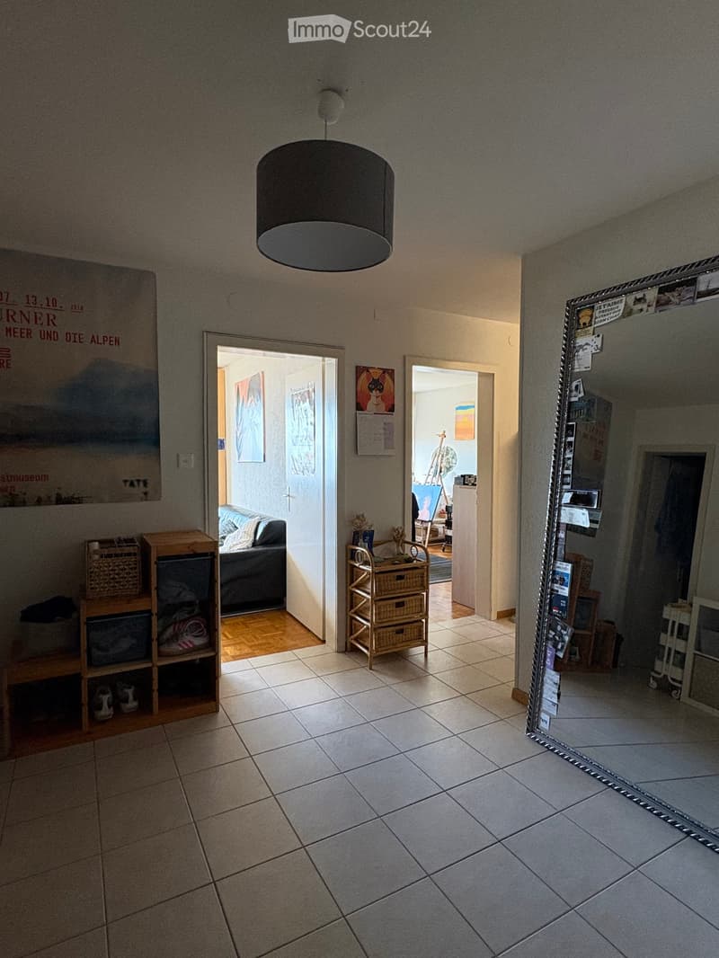 Hallway with tiled floor, pendant light fixture, open doors leading to adjacent rooms, visible furniture in adjacent spaces.