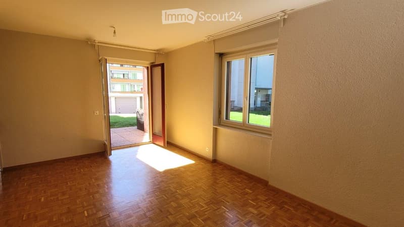 Empty room with wooden flooring, large window, and open sliding door leading to a patio area.