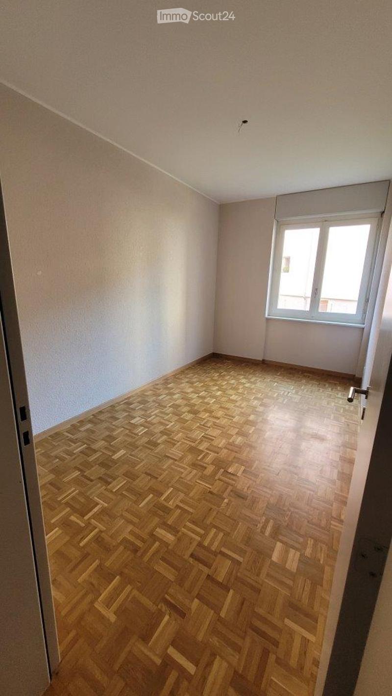Empty room with wooden herringbone flooring, white walls, and a single window with white frame and blinds.