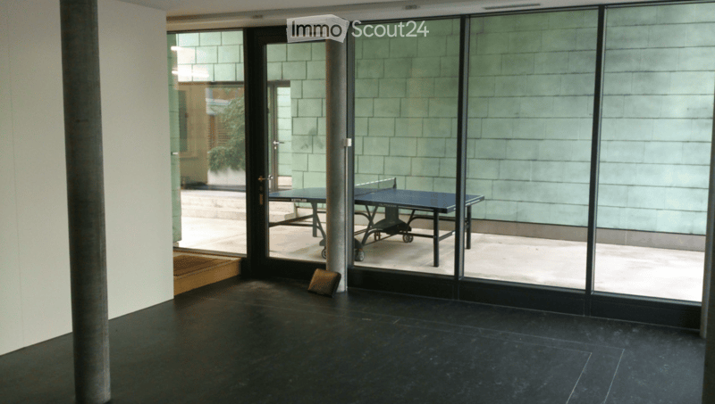 Modern interior with dark flooring, large glass sliding doors leading to an outdoor area, and a small table and chair set near the entrance.