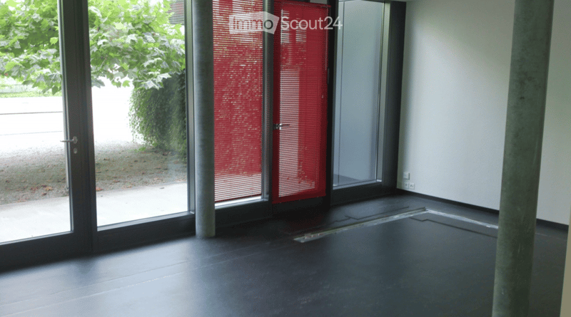 Empty room with dark tiled floor, large sliding glass doors with red blinds, and a view of greenery outside.