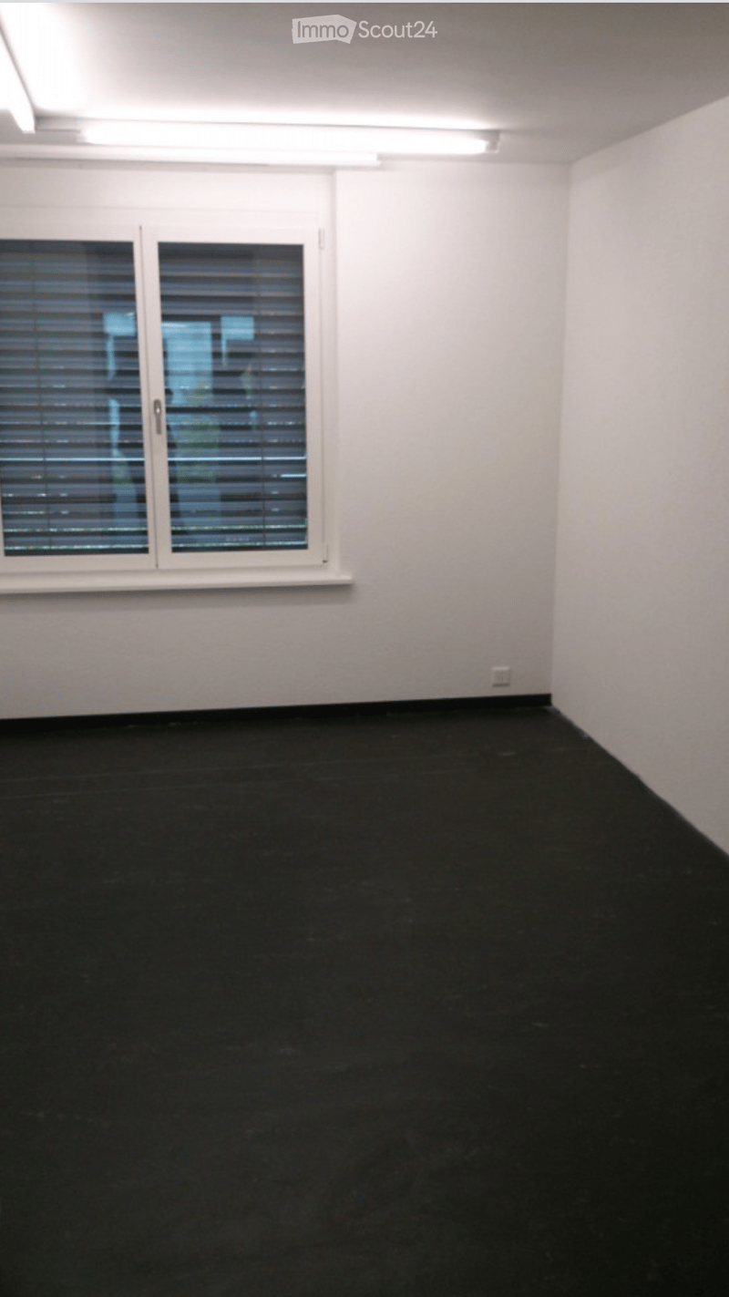 Empty room with white walls, black flooring, and a large window with blinds.