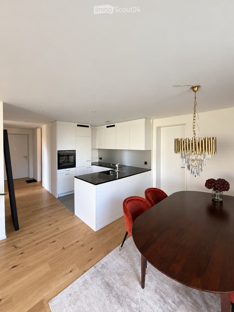 Modern kitchen and dining area with white cabinetry, black countertops, a central island, a dining table with red chairs, and a decorative chandelier.