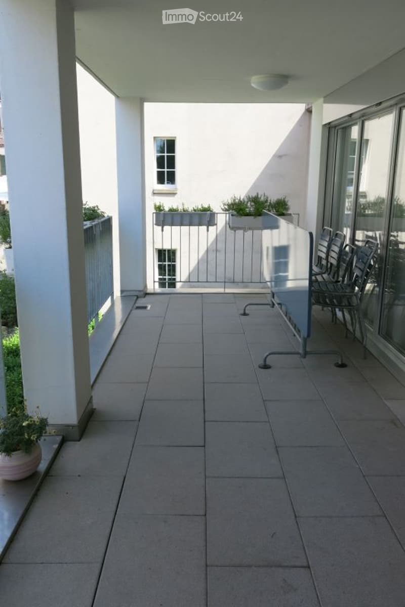 Balcony with tiled floor, white walls, metal railing, and potted plants on the sides.