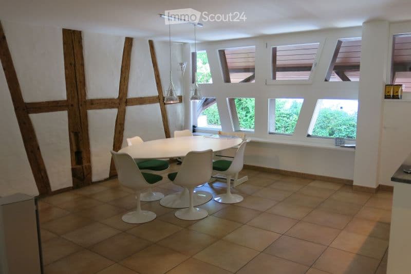 Modern dining room with a white round table, six white chairs, pendant lights, and large windows with wooden shutters.