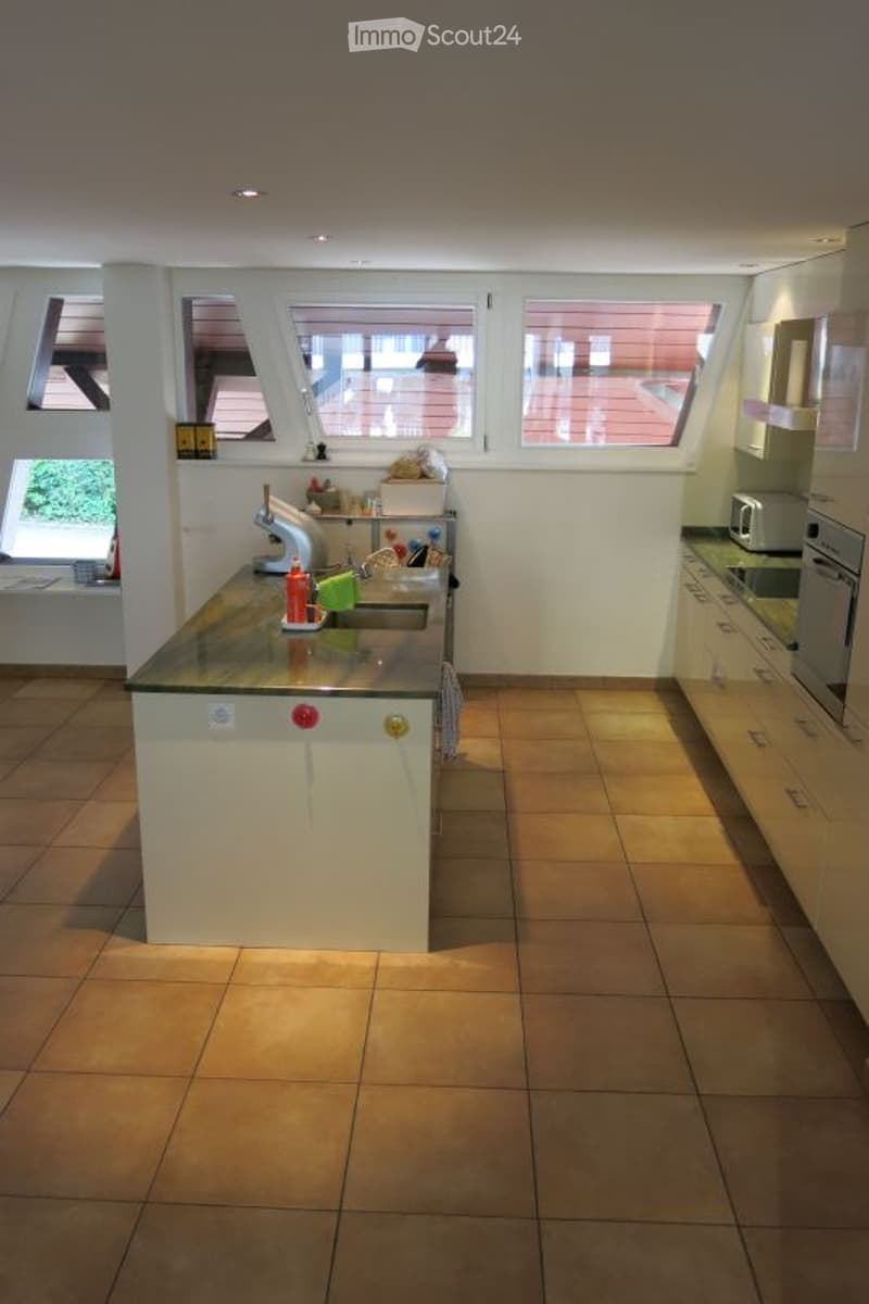 Modern kitchen with white cabinets, tiled floor, and stainless steel appliances. Features a central island with a sink and faucet, microwave, and oven.