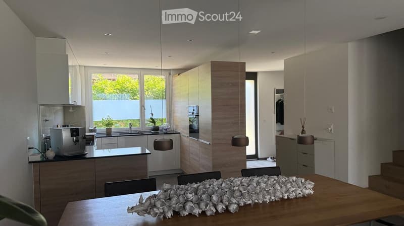 Modern kitchen and dining area with sleek cabinetry, pendant lights, a coffee machine, and a dining table with chairs.
