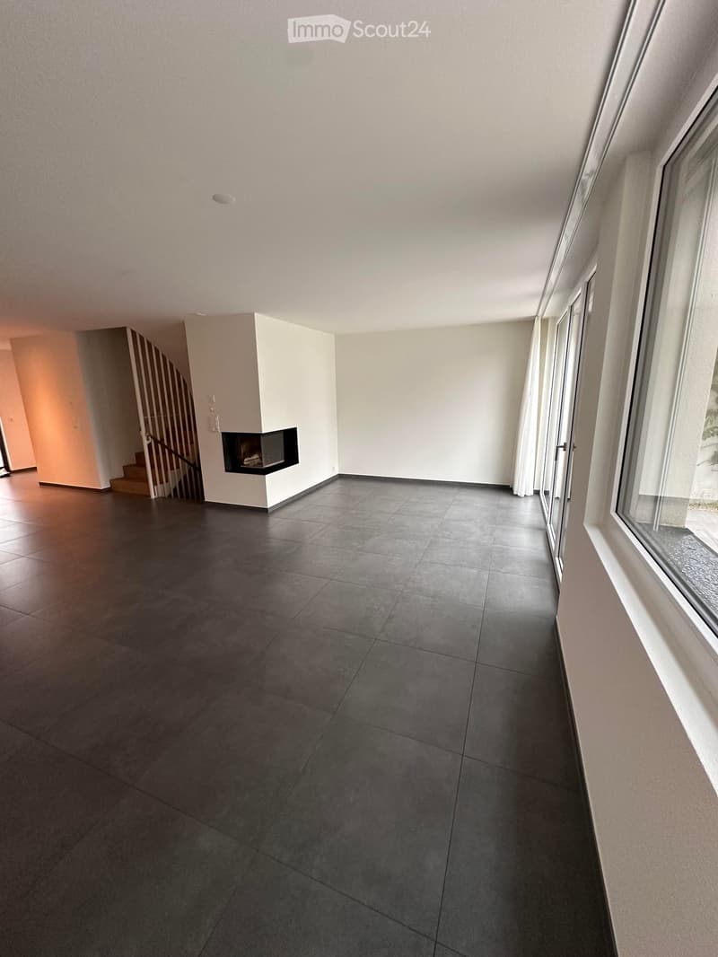 Empty hallway with dark tiled floor, white walls, large windows, and a built-in fireplace on the left side.
