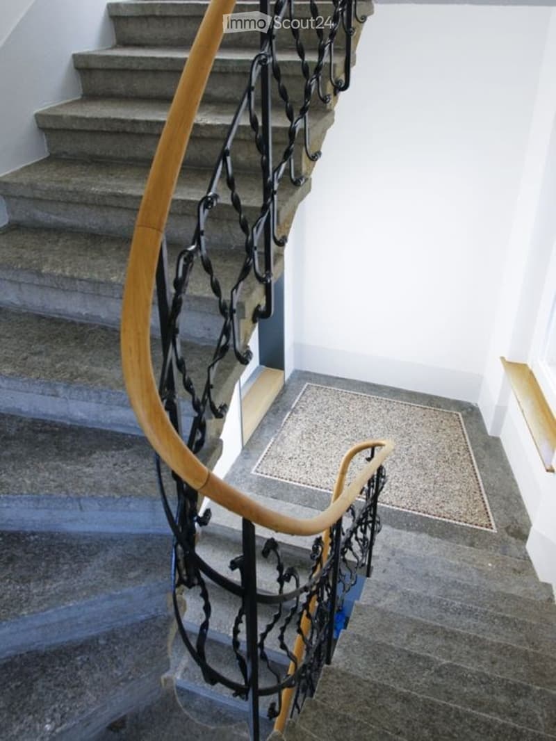 Spiral staircase with wooden handrails and black metal balustrade, leading to an upper level.
