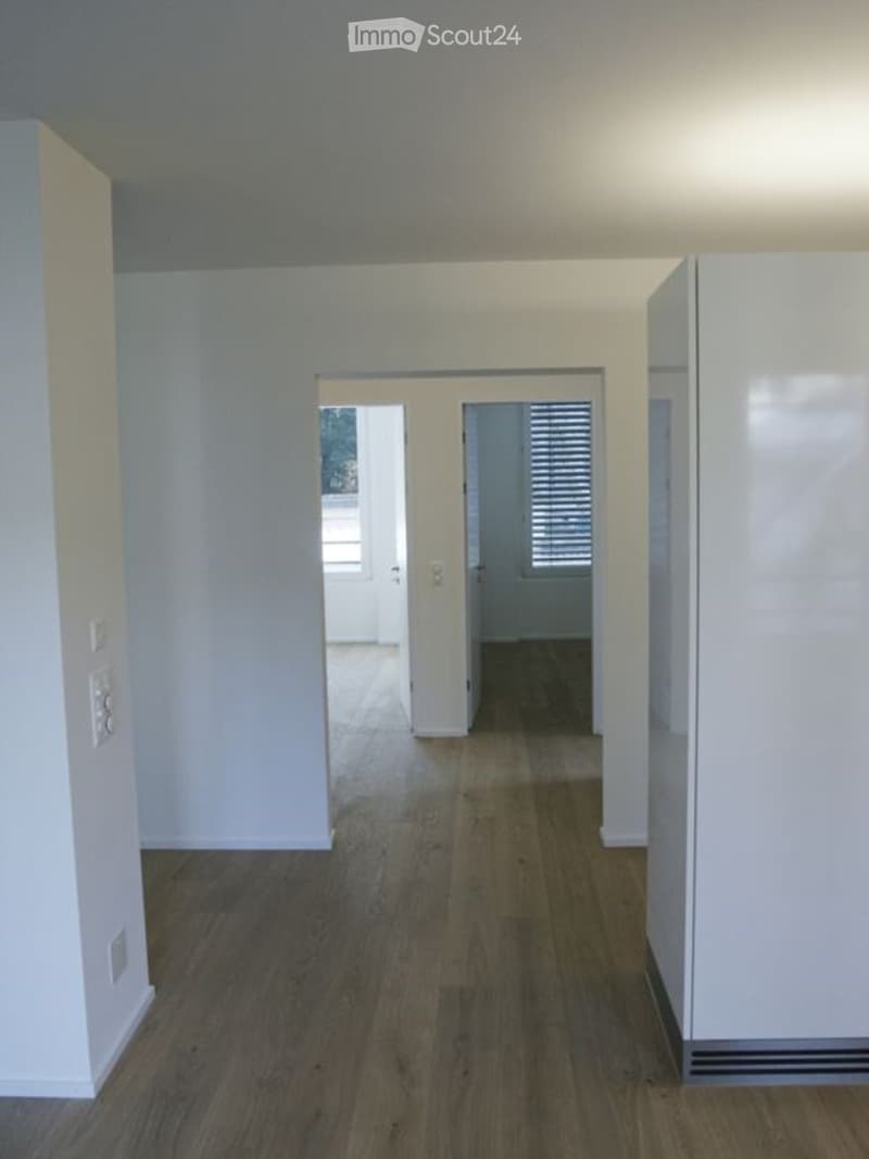 Empty hallway with wooden flooring and white walls, leading to two open doors.