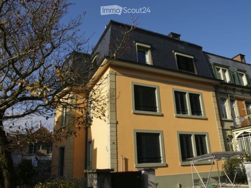 A multi-story residential house with a yellow facade, multiple windows, and a dark roof.