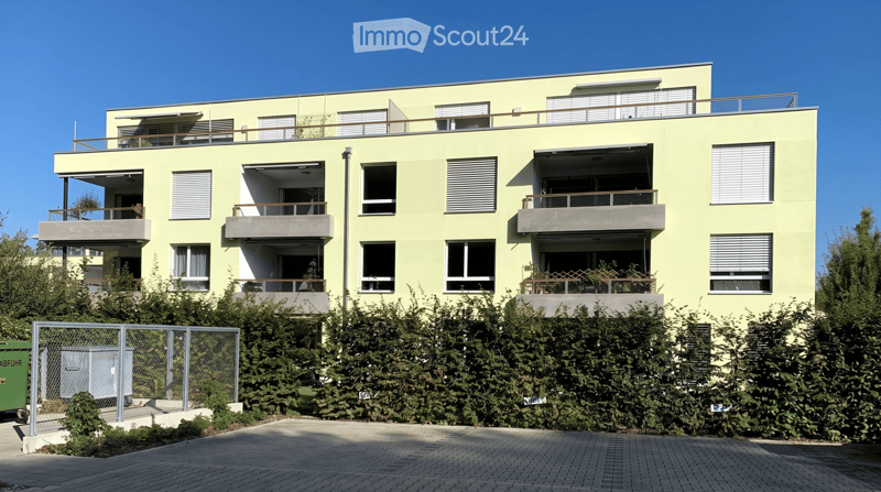 Modern three-story residential building with light yellow facade, multiple balconies, and large windows.