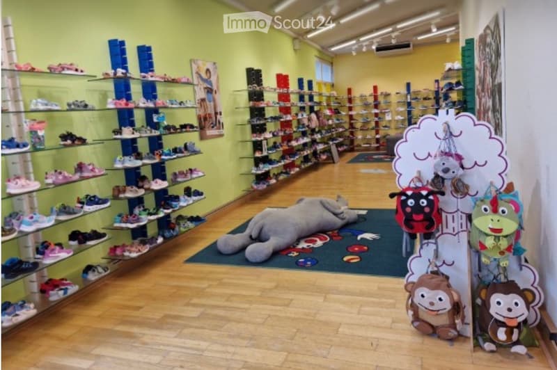 A brightly lit shoe store with multiple shelves displaying various shoes, a large plush toy on the floor, and a colorful display with hanging toys.