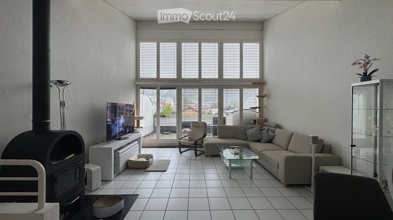 Modern living room with large windows, white tiled floor, grey sectional sofa, glass coffee table, armchair, TV, fireplace, and cat accessories.