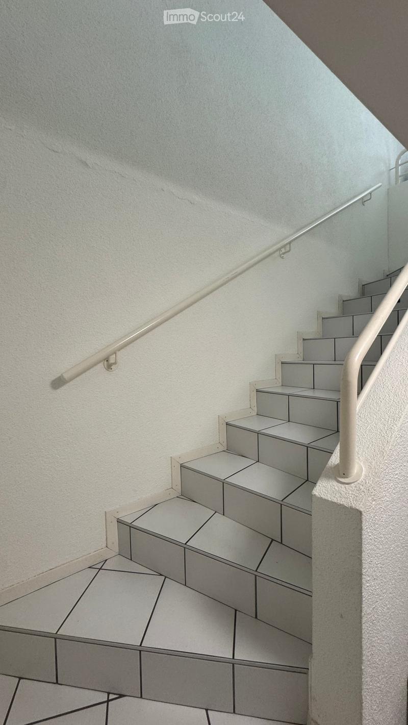 Staircase with grey tiled steps, white textured walls, and white handrails on both sides.