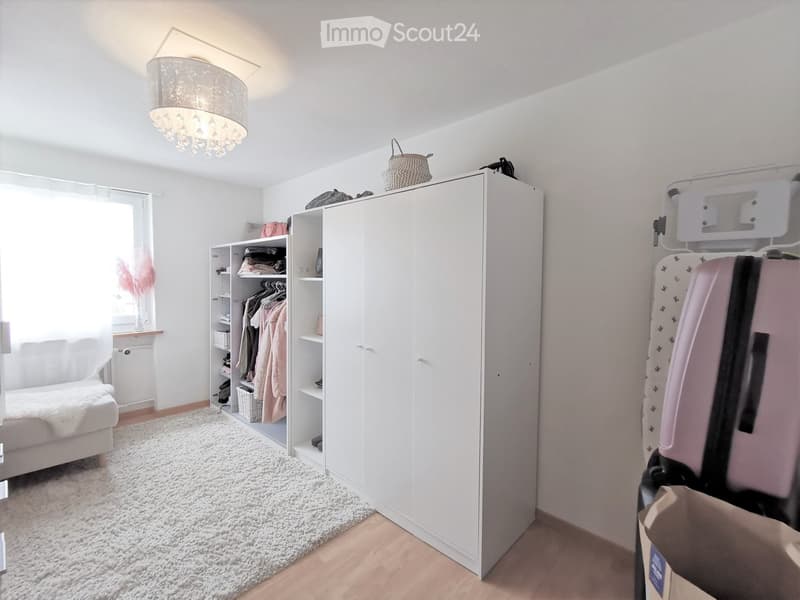 Bright, minimalistic room with a white sofa, large wardrobe, decorative lamp, and scattered items like a suitcase and basket.