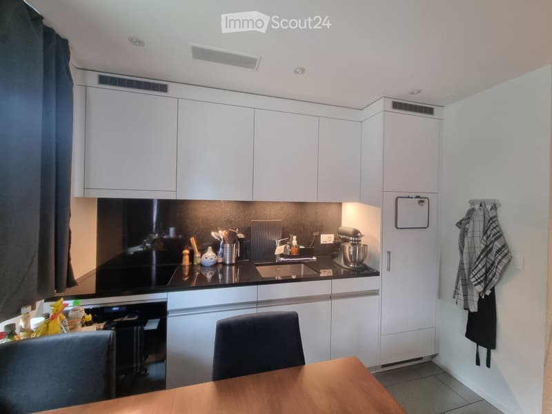 Modern kitchen with white cabinets, black countertop, sink, mixer, and a small dining area with a table and chairs.
