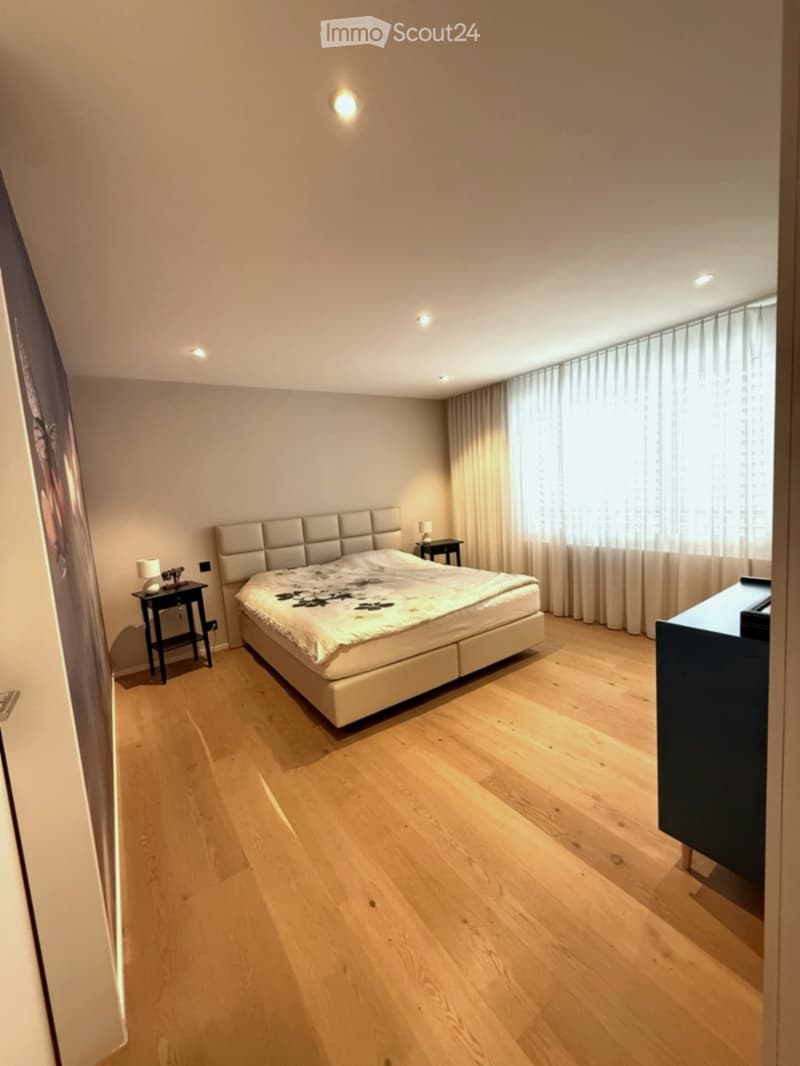 Modern bedroom with a large bed, nightstands, lamps, and large windows with curtains.