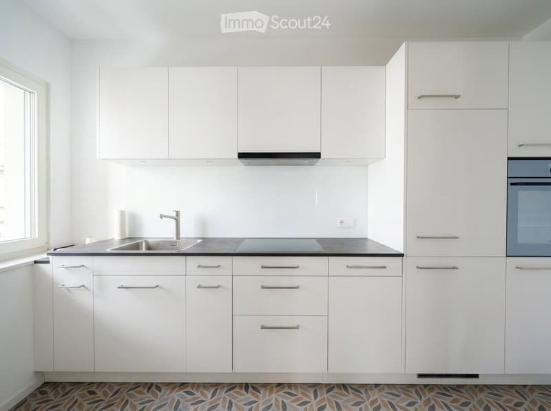 Modern white kitchen with sleek cabinets, stainless steel sink and faucet, built-in oven, and a decorative patterned tile floor.
