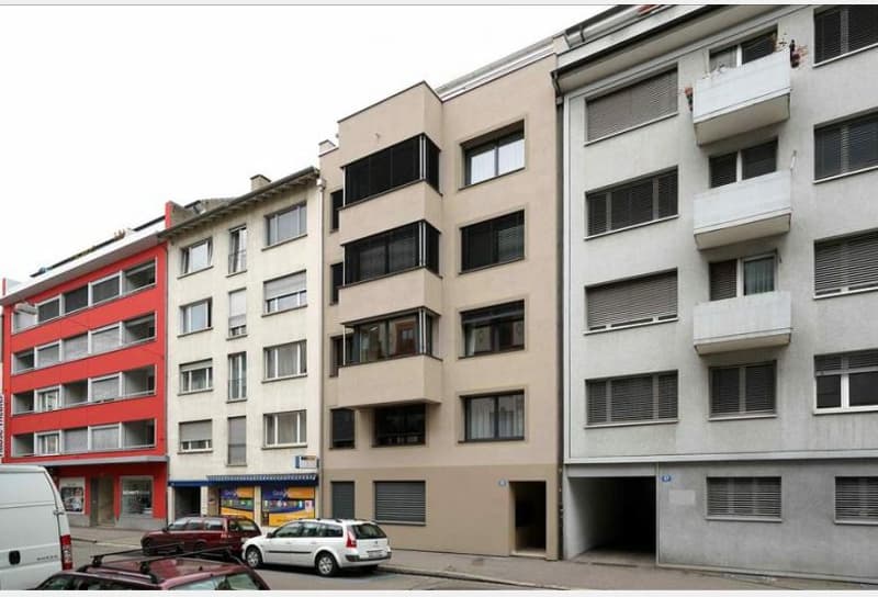 Multi-story residential building with beige and red facades, multiple windows, balconies, and a visible garage entrance.