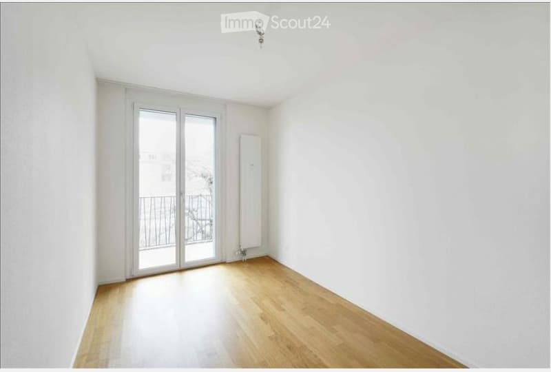 Empty room with wooden flooring, white walls, and a large glass door leading to a balcony.