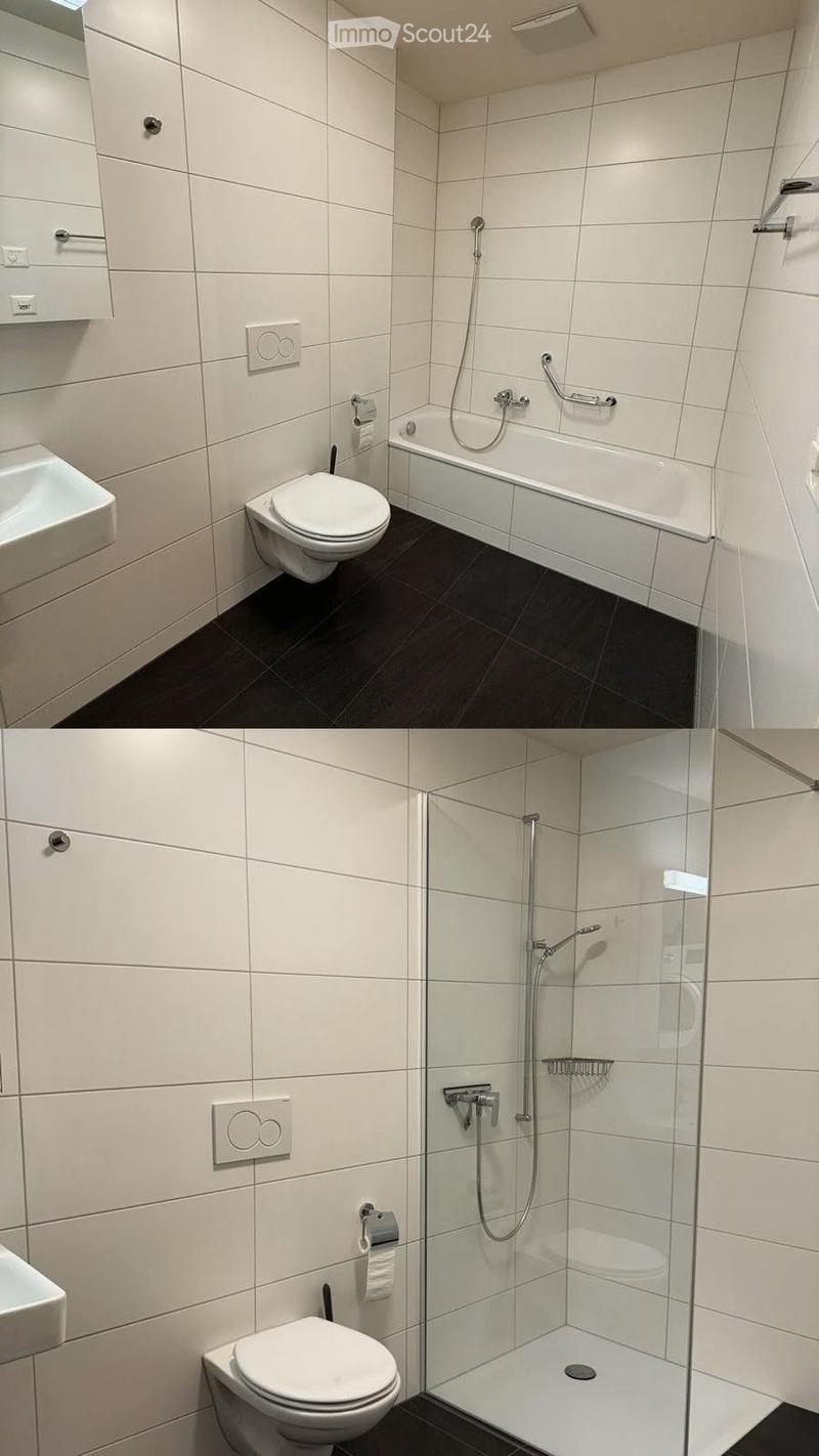 Modern bathroom with white tiles, dark floor, toilet, bathtub, shower, sink, and mirror.