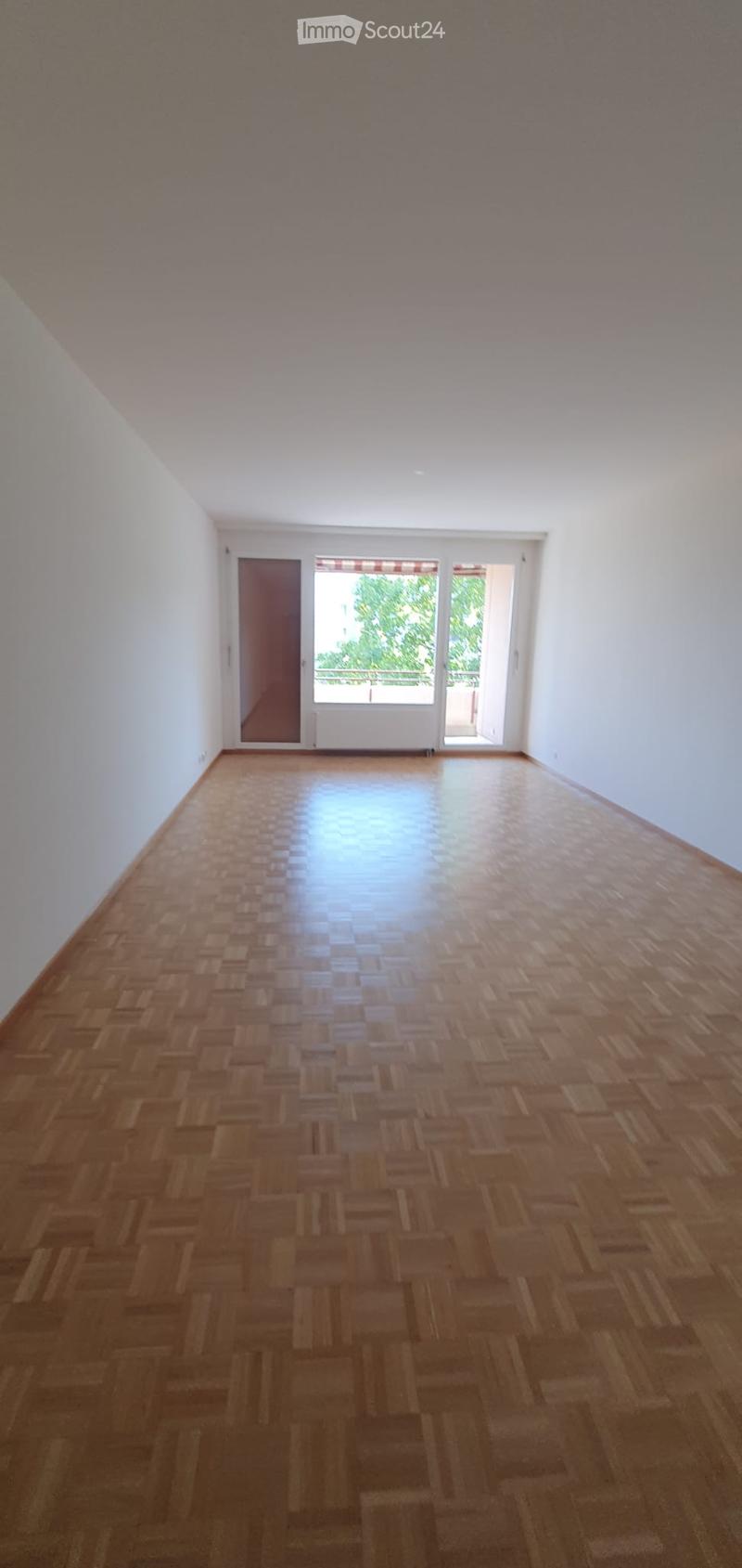 Empty room with wooden parquet flooring, white walls, and large windows with blinds. No furniture or equipment present.