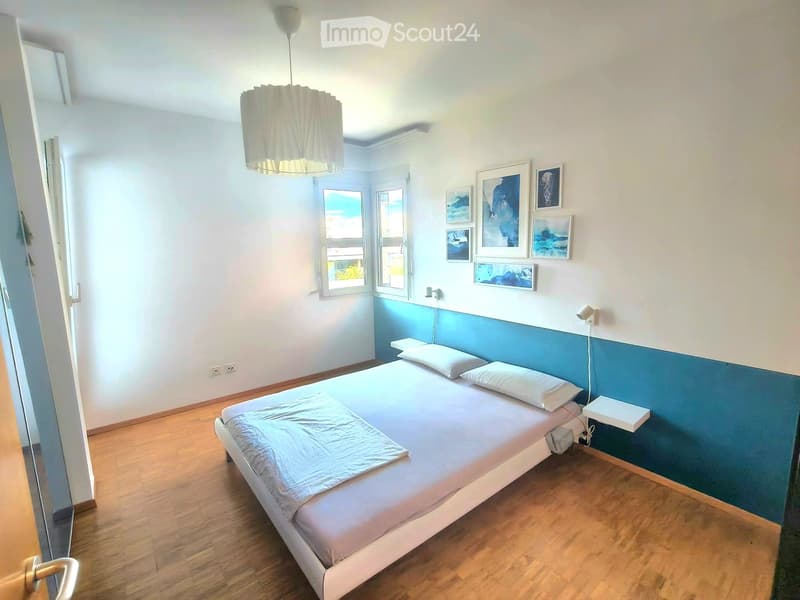 Cozy bedroom with a single bed, white bedding, wooden floor, and wall-mounted nightstand. Features a blue accent wall and several framed pictures.