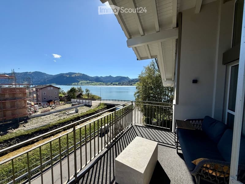 Balcony with a view of a lake and mountains, featuring a sofa and a small table.