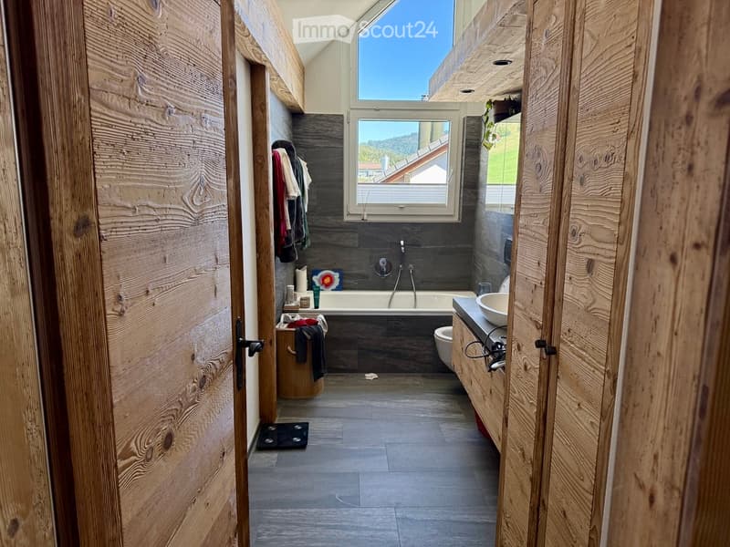 Modern bathroom with wooden walls, a bathtub, sink, toilet, and a large window offering a scenic view.