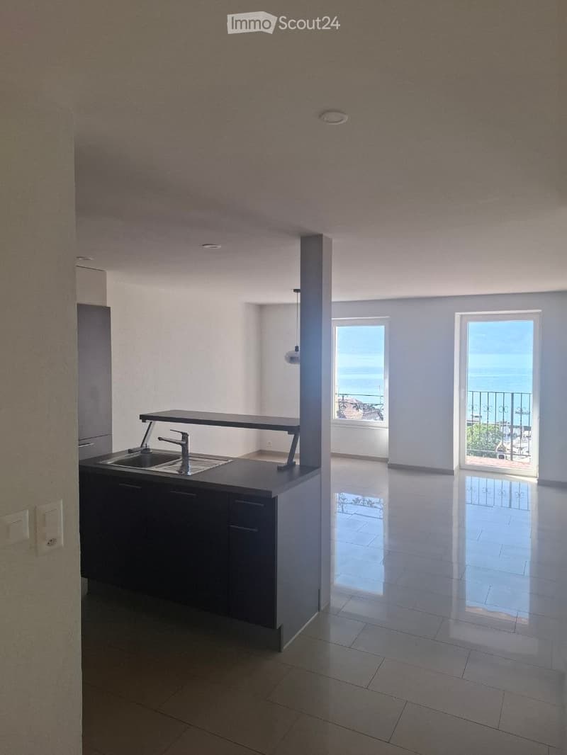 Empty kitchen area with a sink, countertop, and a view of a balcony overlooking the sea.