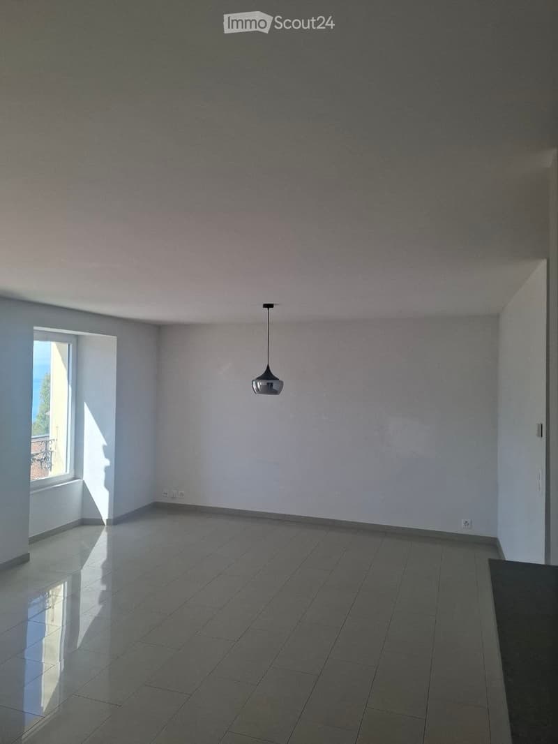 Empty room with tiled floor, white walls, and a single pendant light fixture. Natural light enters through a window on the left side.
