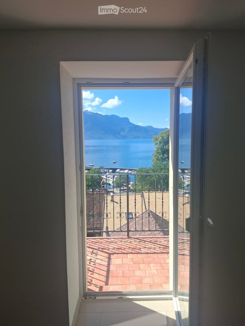 Open balcony with a view of a lake and mountains, featuring a metal railing and tiled floor.