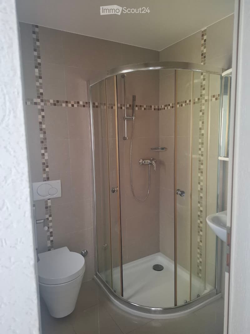 Modern bathroom with a corner shower, toilet, and sink. Features tiled walls with decorative mosaic borders and a glass shower enclosure.