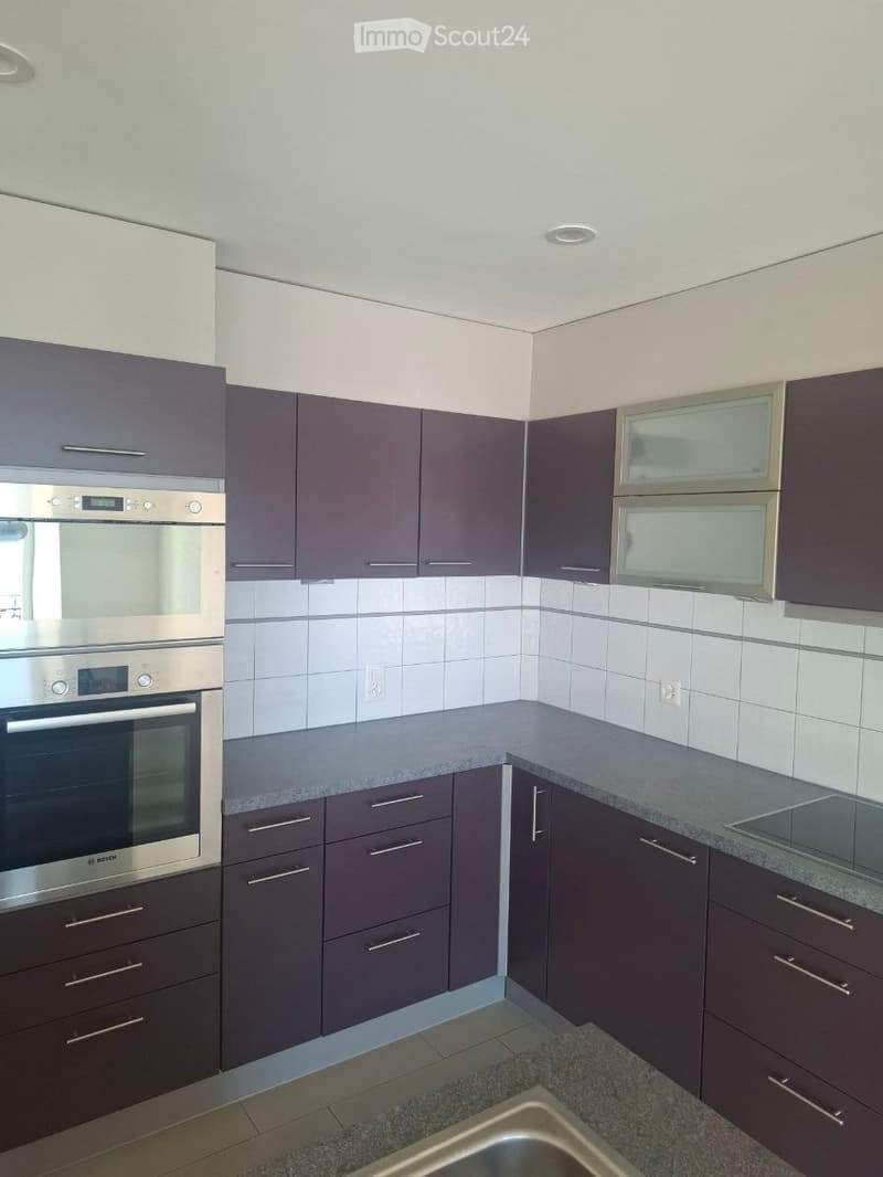 Modern kitchen with dark grey cabinets, stainless steel oven, granite countertop, and built-in sink.