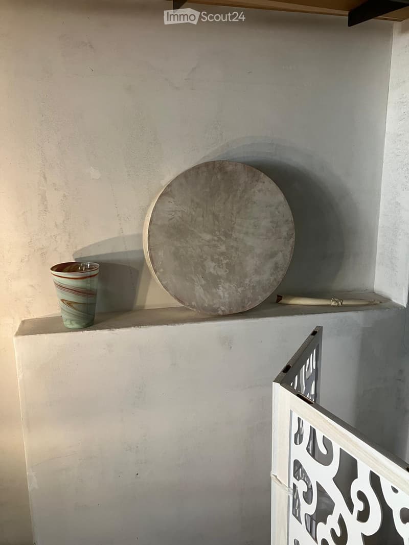 A simple hallway with a white railing and a shelf holding a ceramic cup and a large round plate.