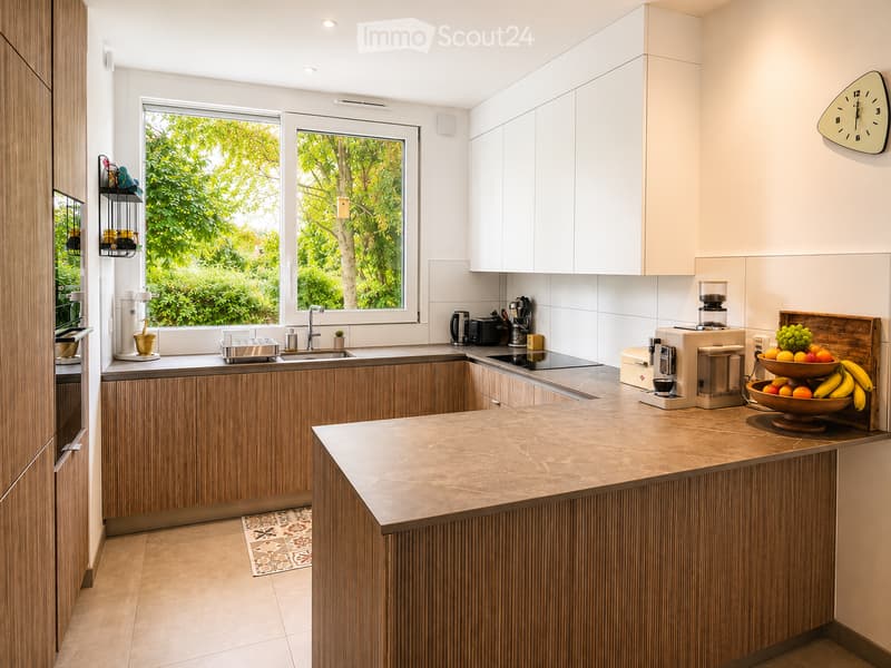 Modern kitchen with wooden cabinets, white upper cabinets, and a central island. Features include a sink, coffee maker, fruit bowl, and various appliances.