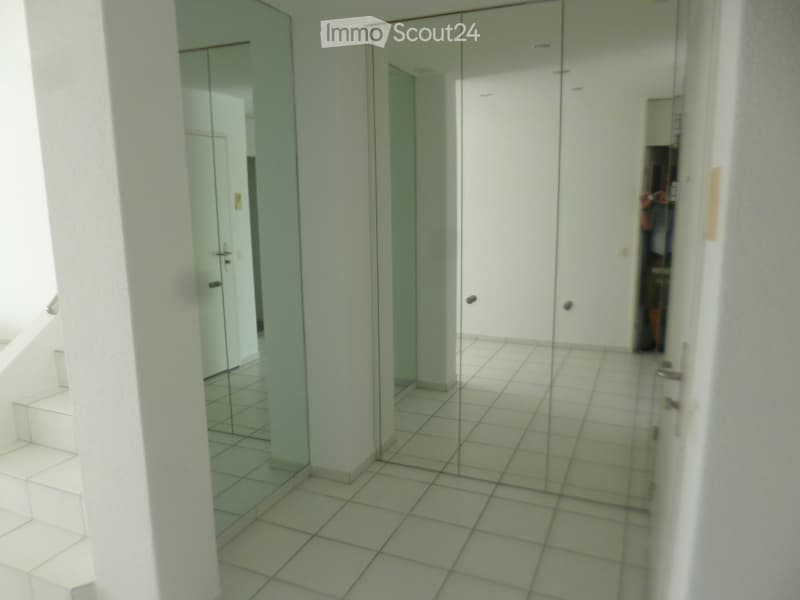 A clean, tiled hallway with white walls, a glass door, and a staircase leading upwards.