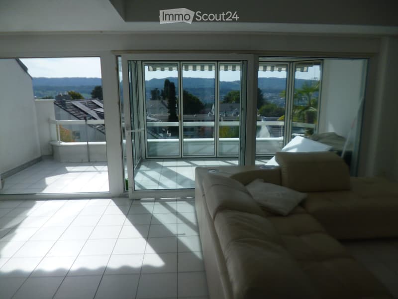 Bright living room with large sliding glass doors leading to a balcony, tiled floor, and a beige sofa with cushions.