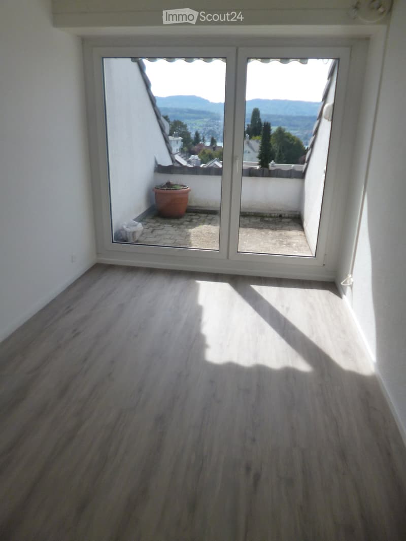 Empty room with wooden flooring and large sliding glass doors leading to a balcony with a view of the landscape.
